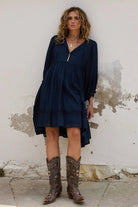 Woman wearing a navy dress and brown boots against a textured wall.