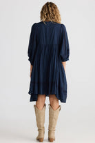 Person wearing a navy dress with long sleeves and a white background back