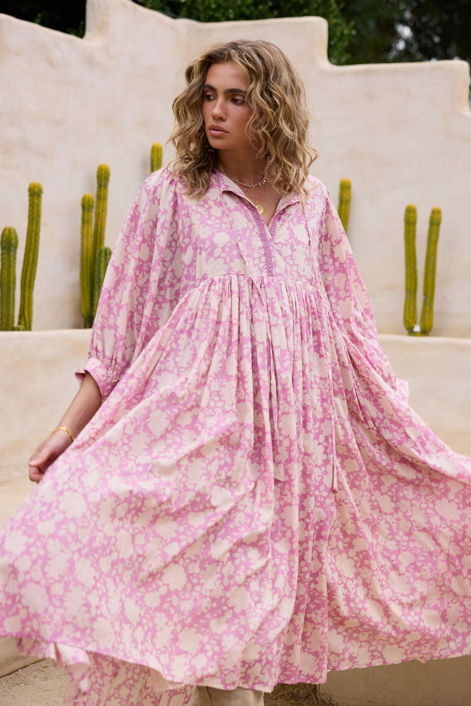Woman wearing a pink floral dress standing outdoors with cacti in the background