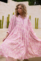 Woman wearing a pink floral dress standing outdoors with cacti in the background