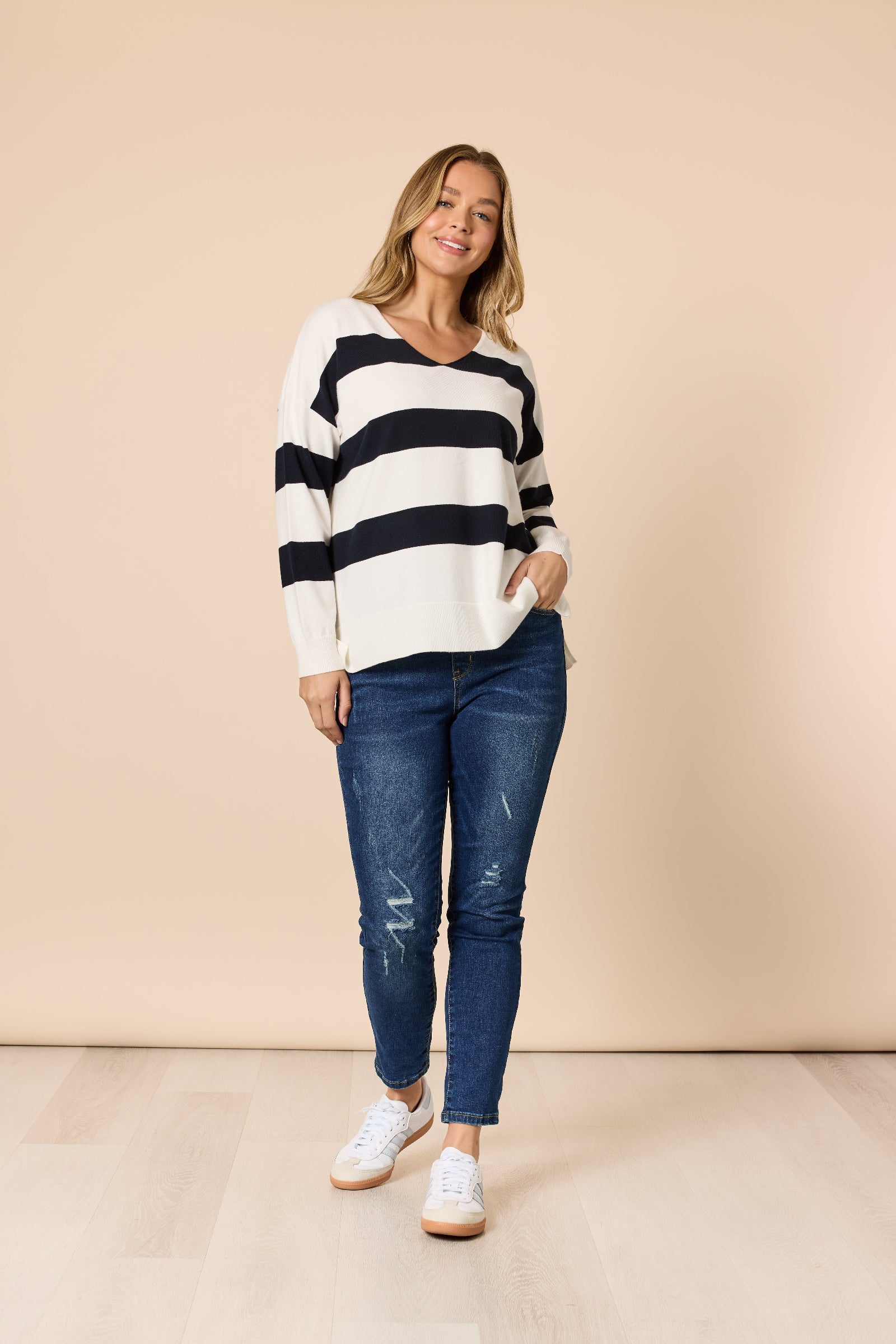 Woman wearing a black and white striped sweater and blue jeans against a beige background