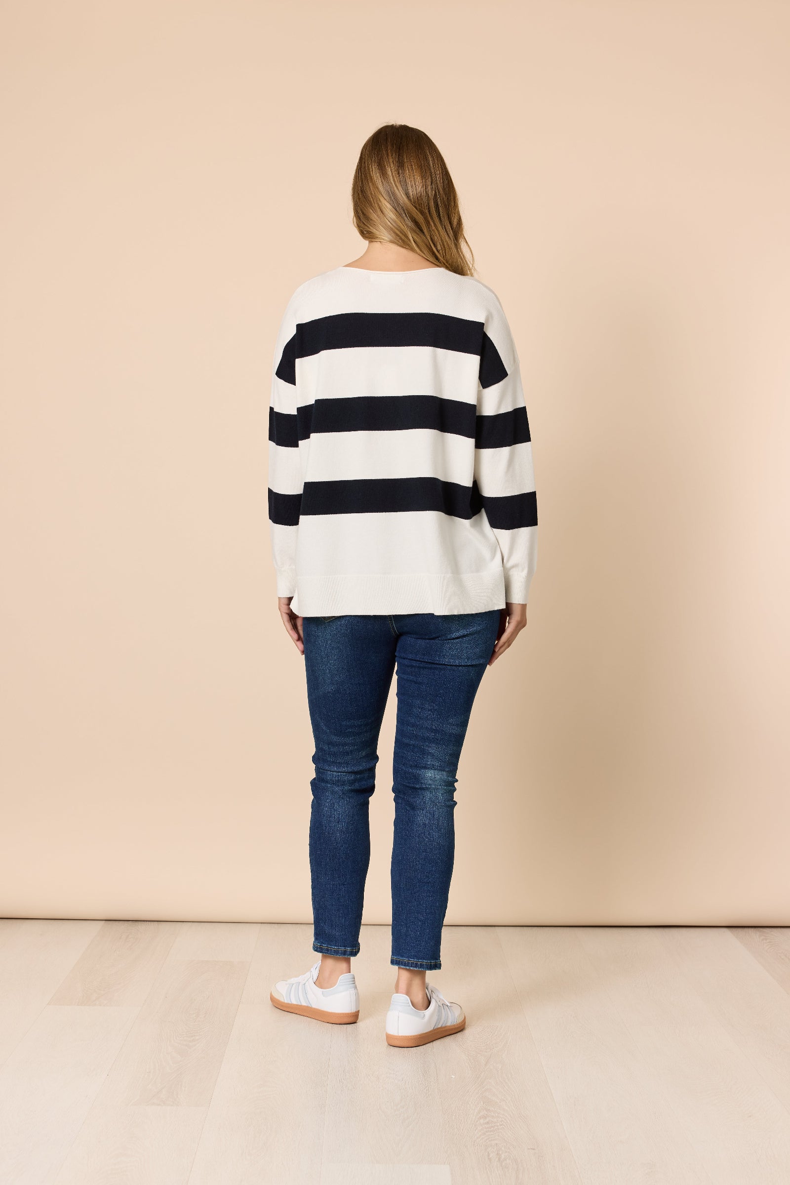 Person wearing a striped sweater and jeans against a beige background