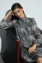 Woman wearing a patterned dress sitting on a chair against a white wall