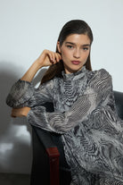 Woman wearing a patterned dress sitting on a chair against a plain background