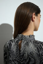 Person wearing a black and white patterned blouse with a plain background back angle
