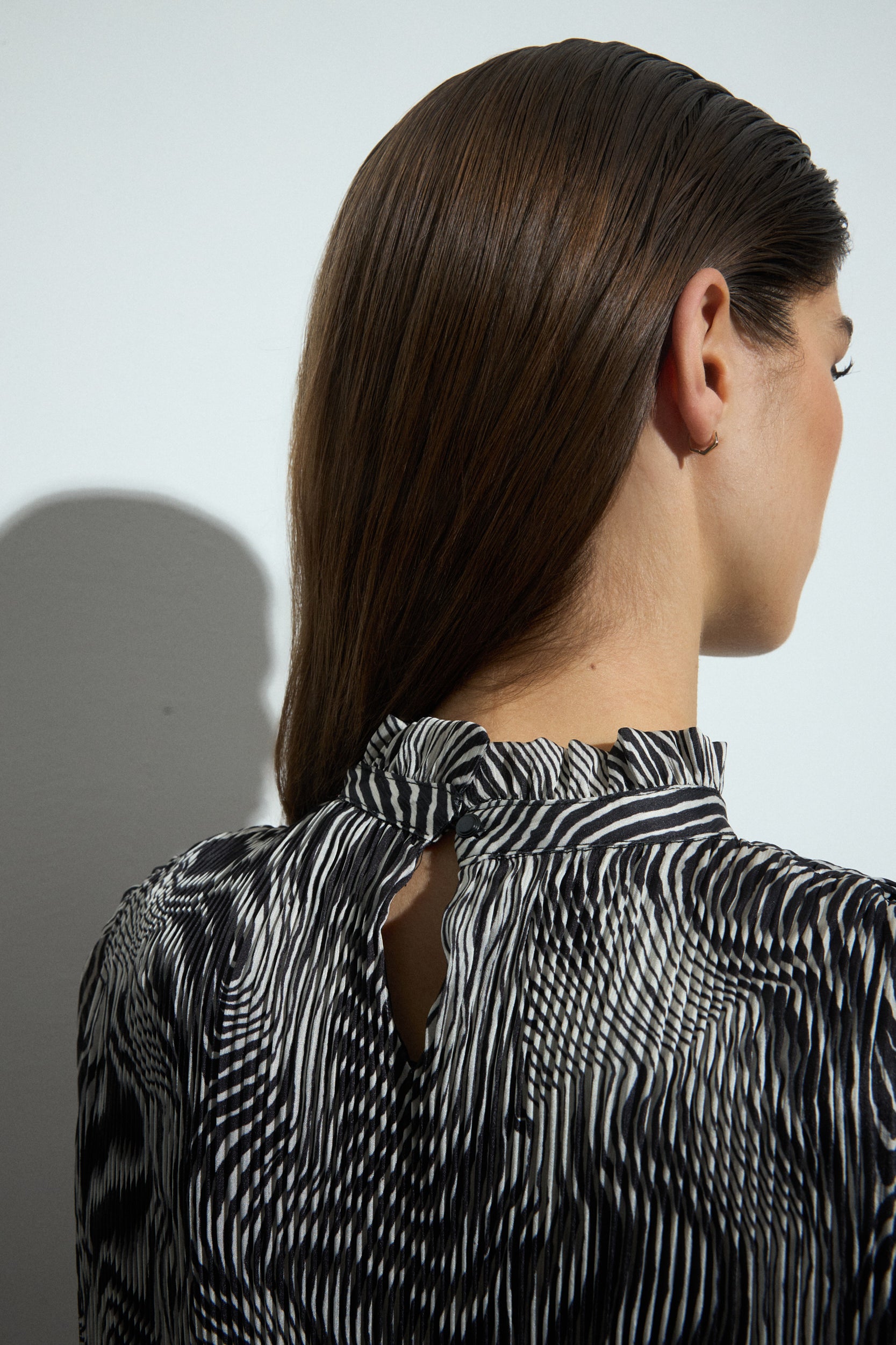 Person wearing a black and white patterned blouse with a plain background back angle