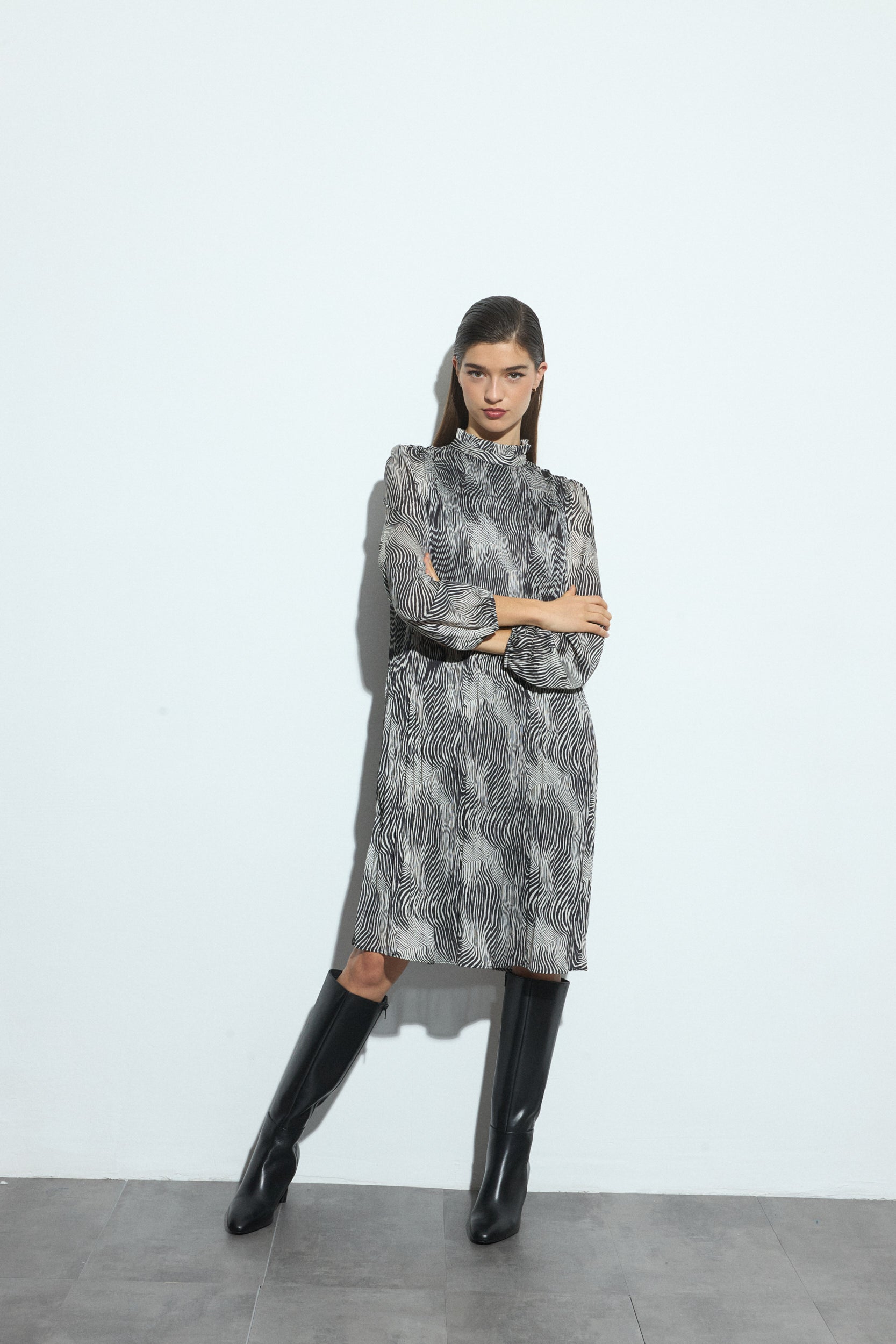 Woman wearing a black and white patterned dress and black boots on a white background