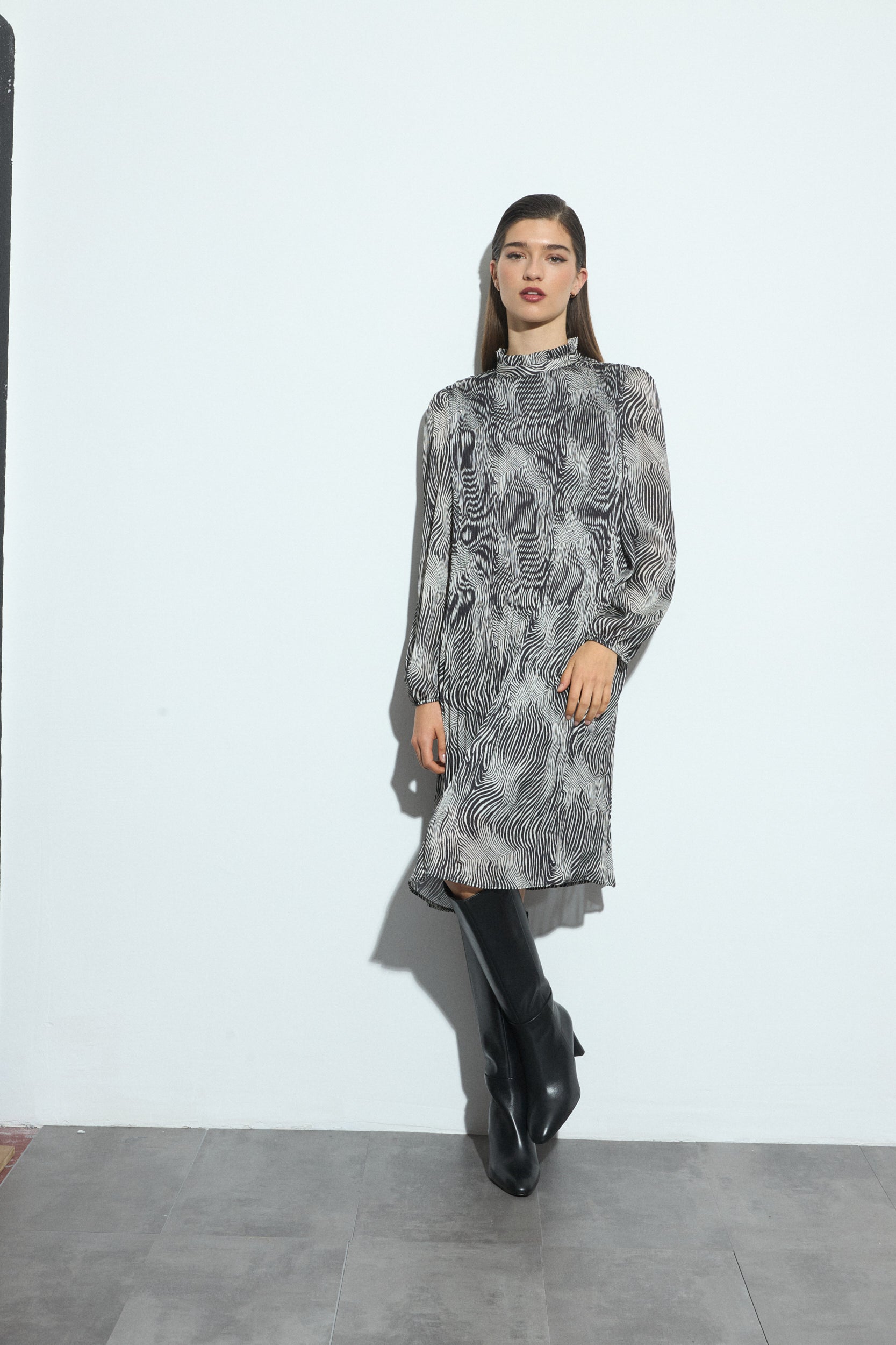 Woman wearing a black and white patterned dress and black boots on a white background