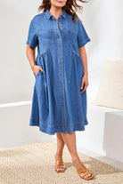 Woman wearing a blue denim dress standing on a textured surface with a white background