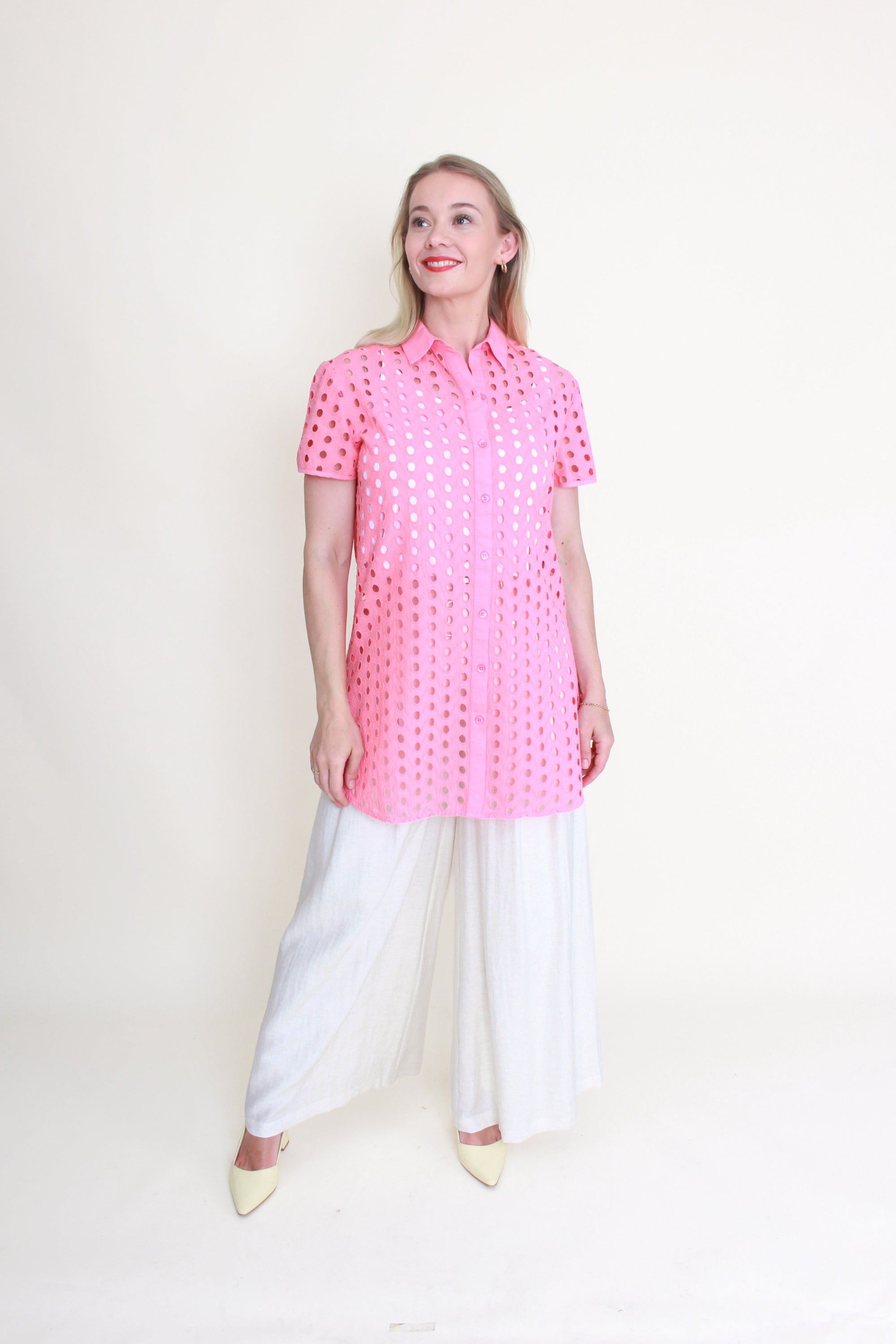 Woman wearing a pink anglaise shirt and white pants on a white background