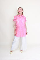 Woman wearing a pink anglaise shirt and white pants on a white background