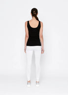 Person wearing a black tank top and white pants on a white background