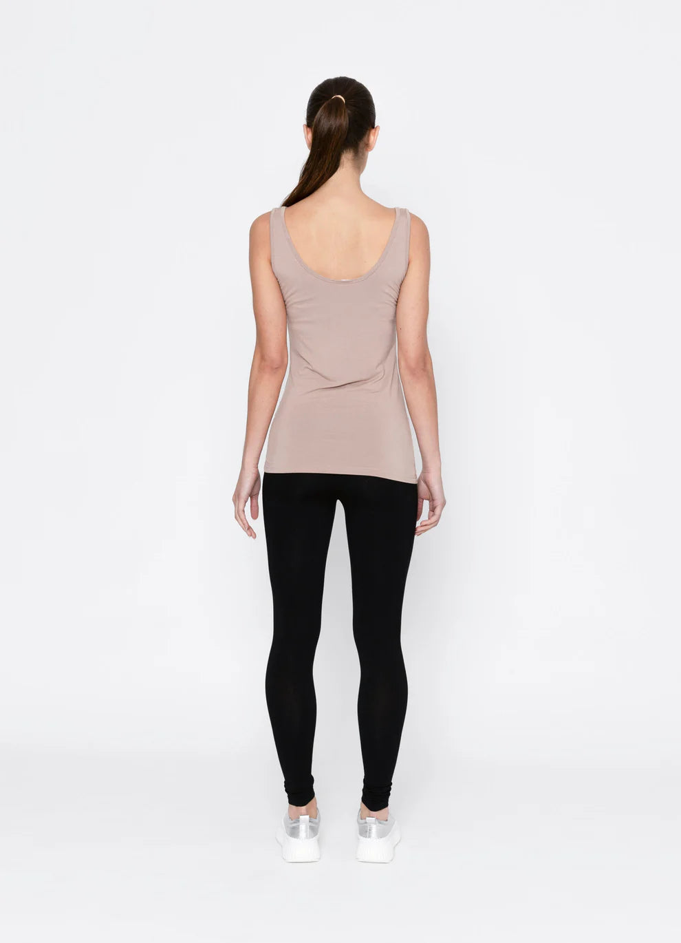 Person wearing a beige tank top and black leggings on a white background