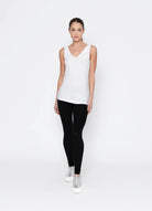 Woman wearing a white sleeveless top and black leggings on a white background