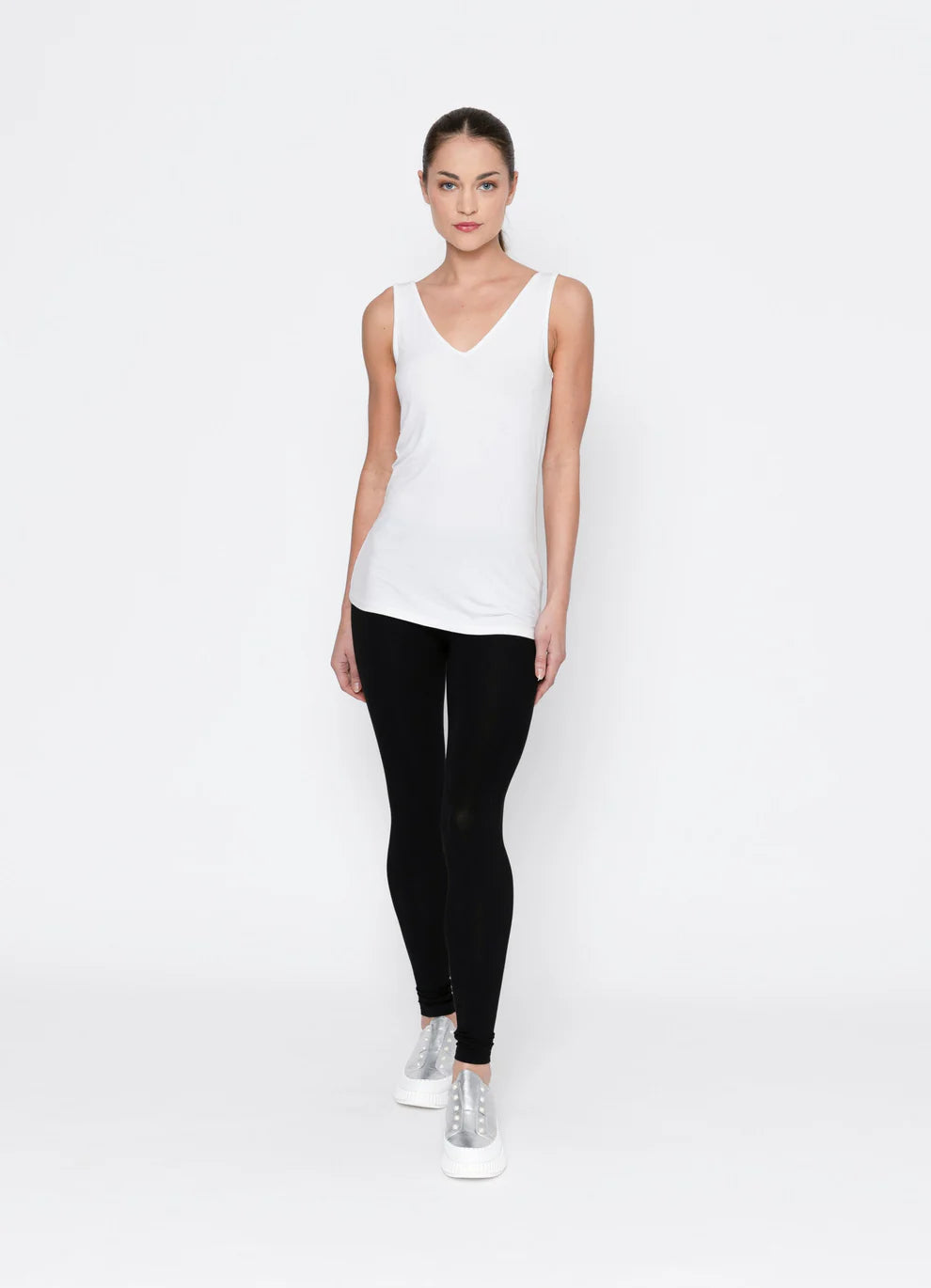 Woman wearing a white sleeveless top and black leggings on a white background