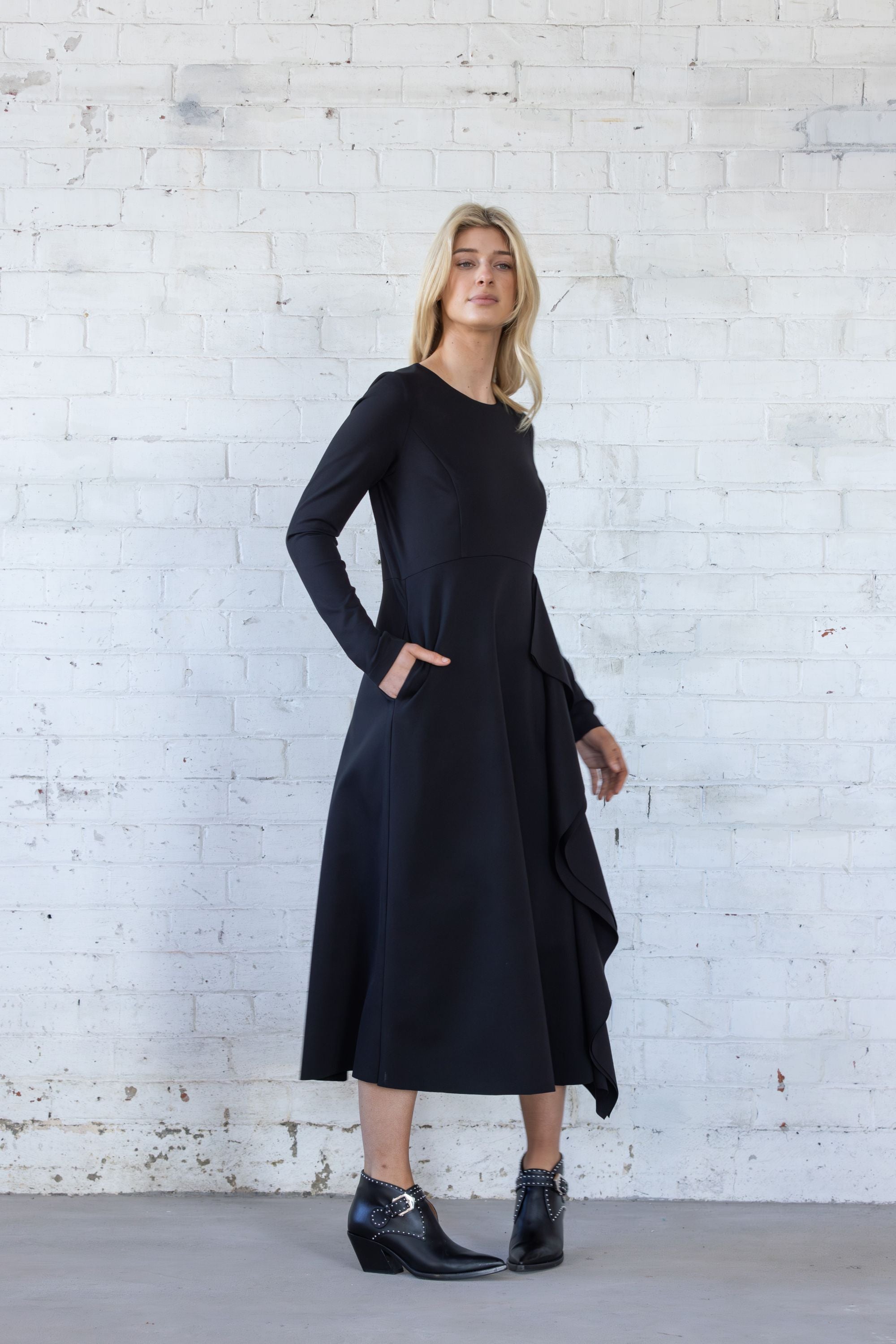 Woman wearing a black dress standing against a white brick wall.