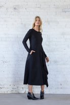 Woman wearing a black dress standing against a white brick wall.