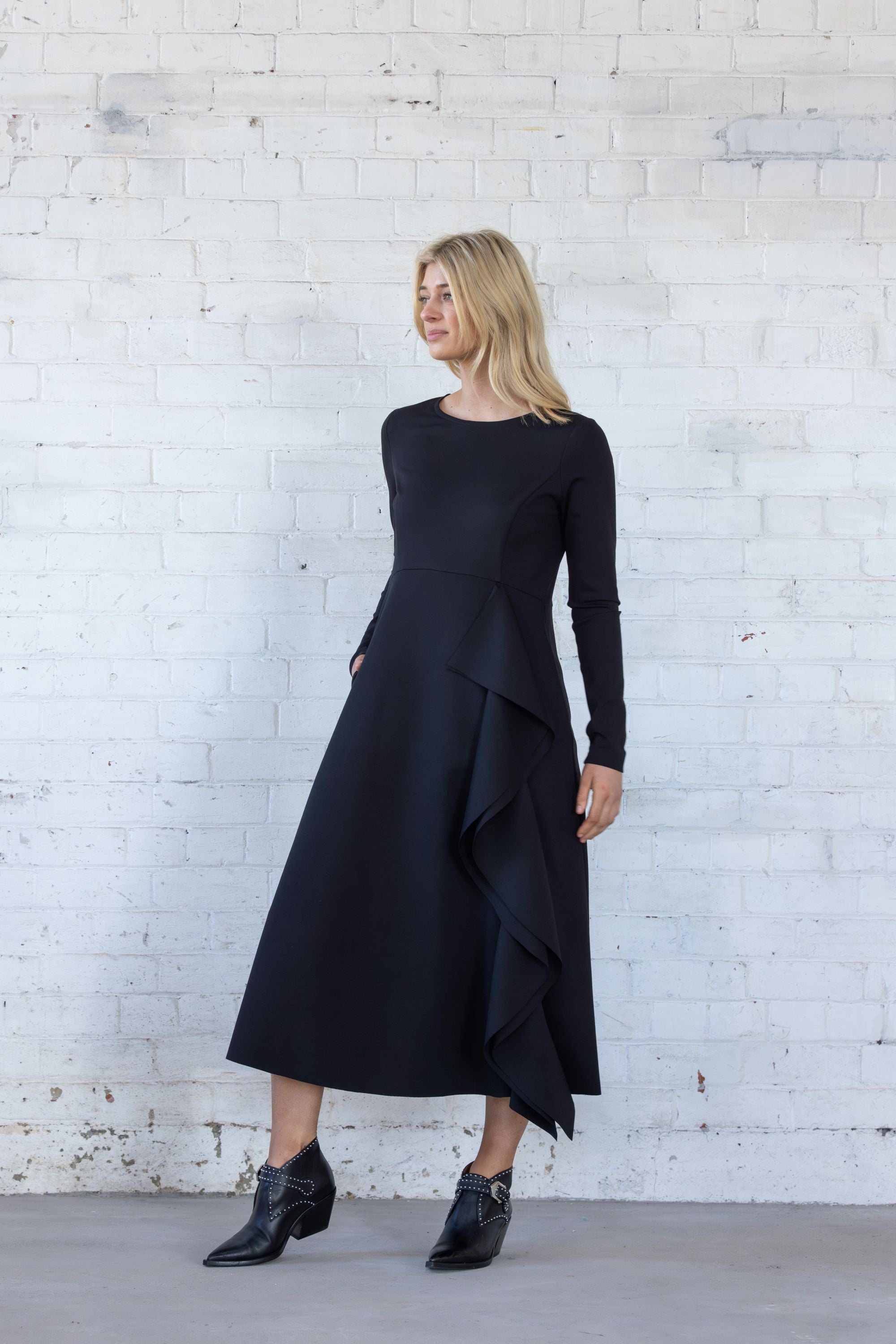 Woman wearing a black dress standing against a white brick wall.
