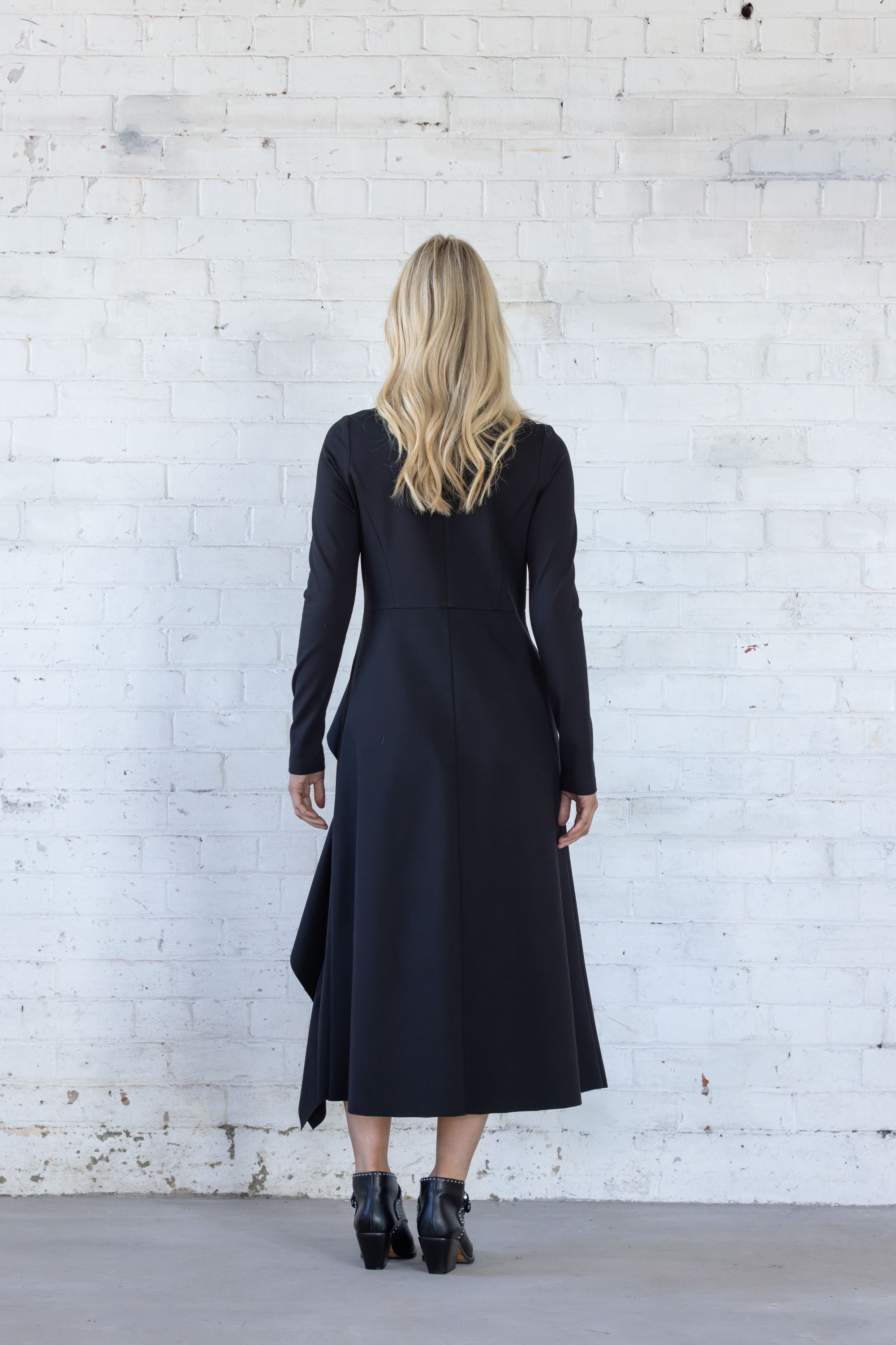 Woman wearing a black dress standing against a white brick wall.