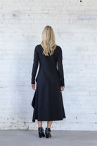 Woman wearing a black dress standing against a white brick wall.