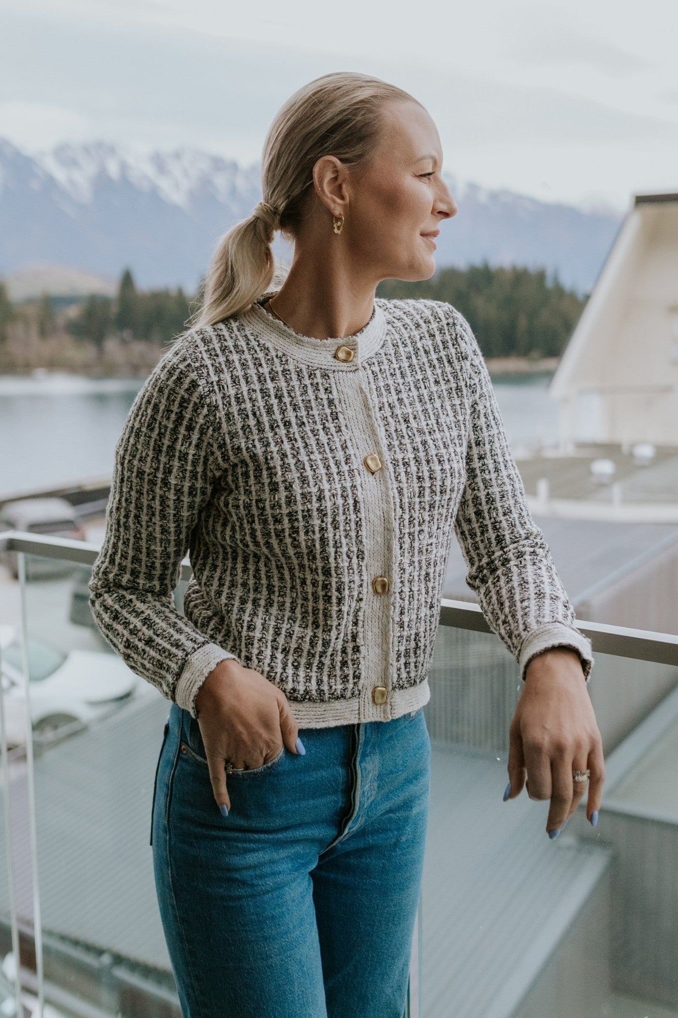Woman wearing check cardigan and blue jeans standing on a balcony 