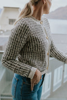 Woman wearing cream check cardigan and blue jeans standing on balcony