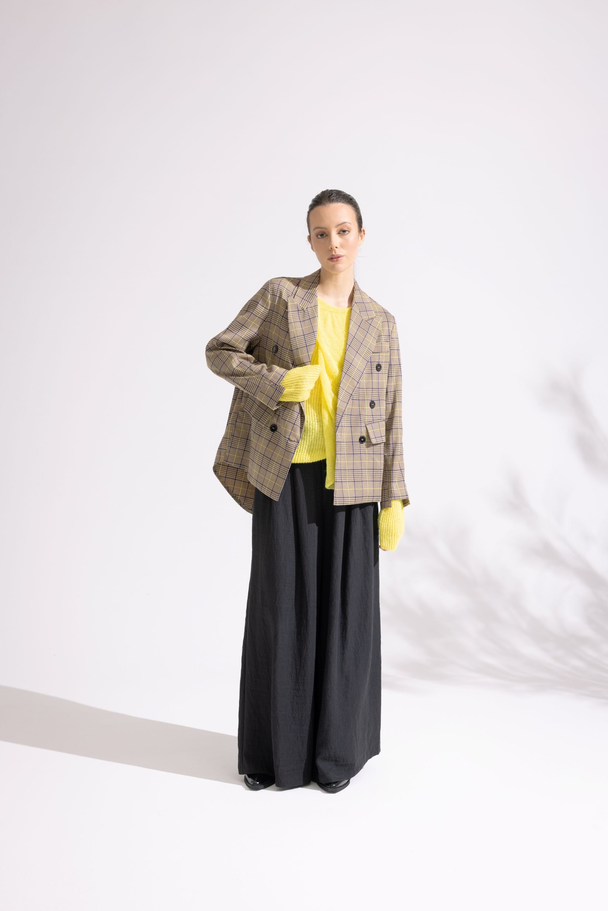Person wearing a plaid blazer, yellow top, and black pants on a white background