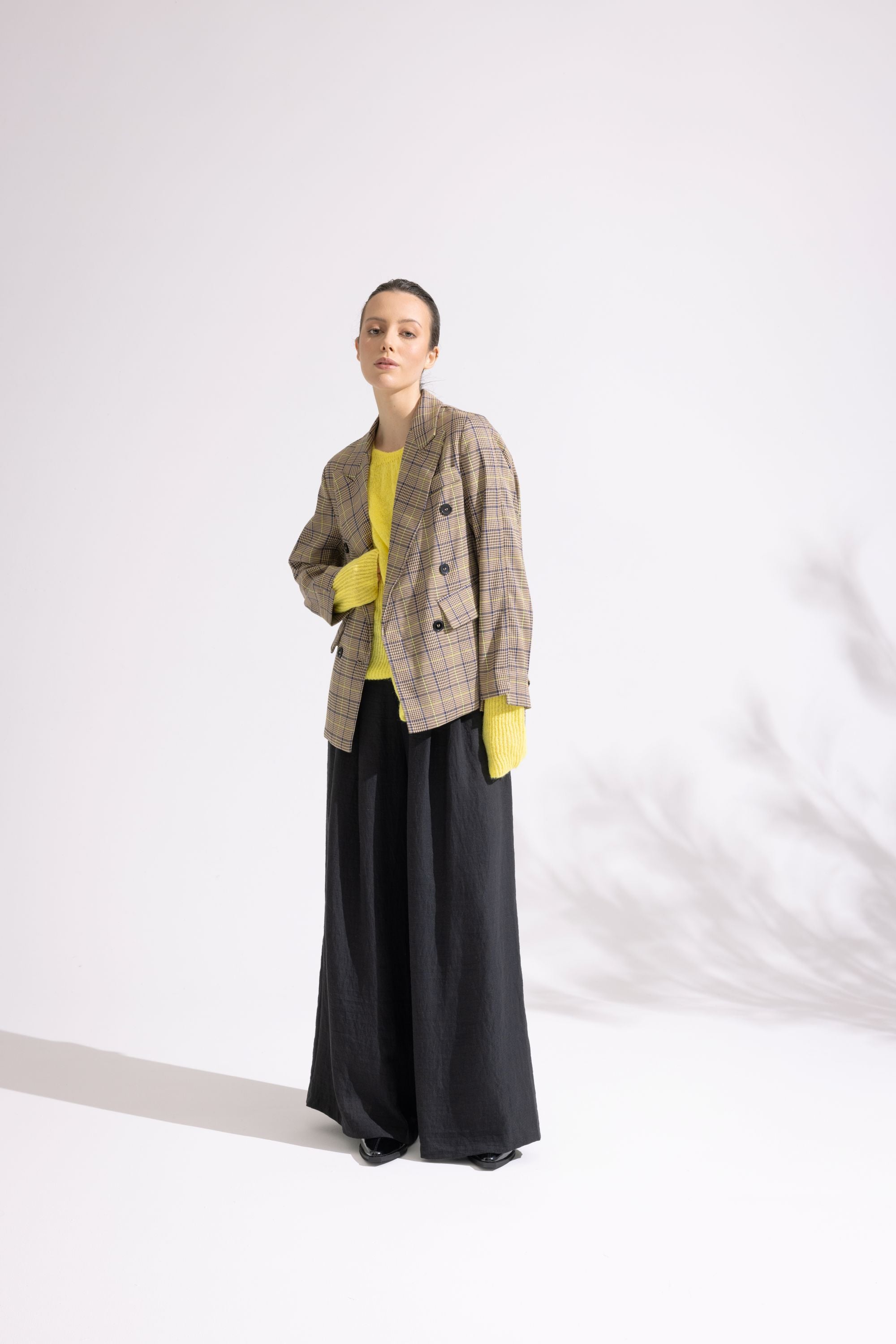 Person wearing a plaid jacket, yellow top, and black pants on a white background