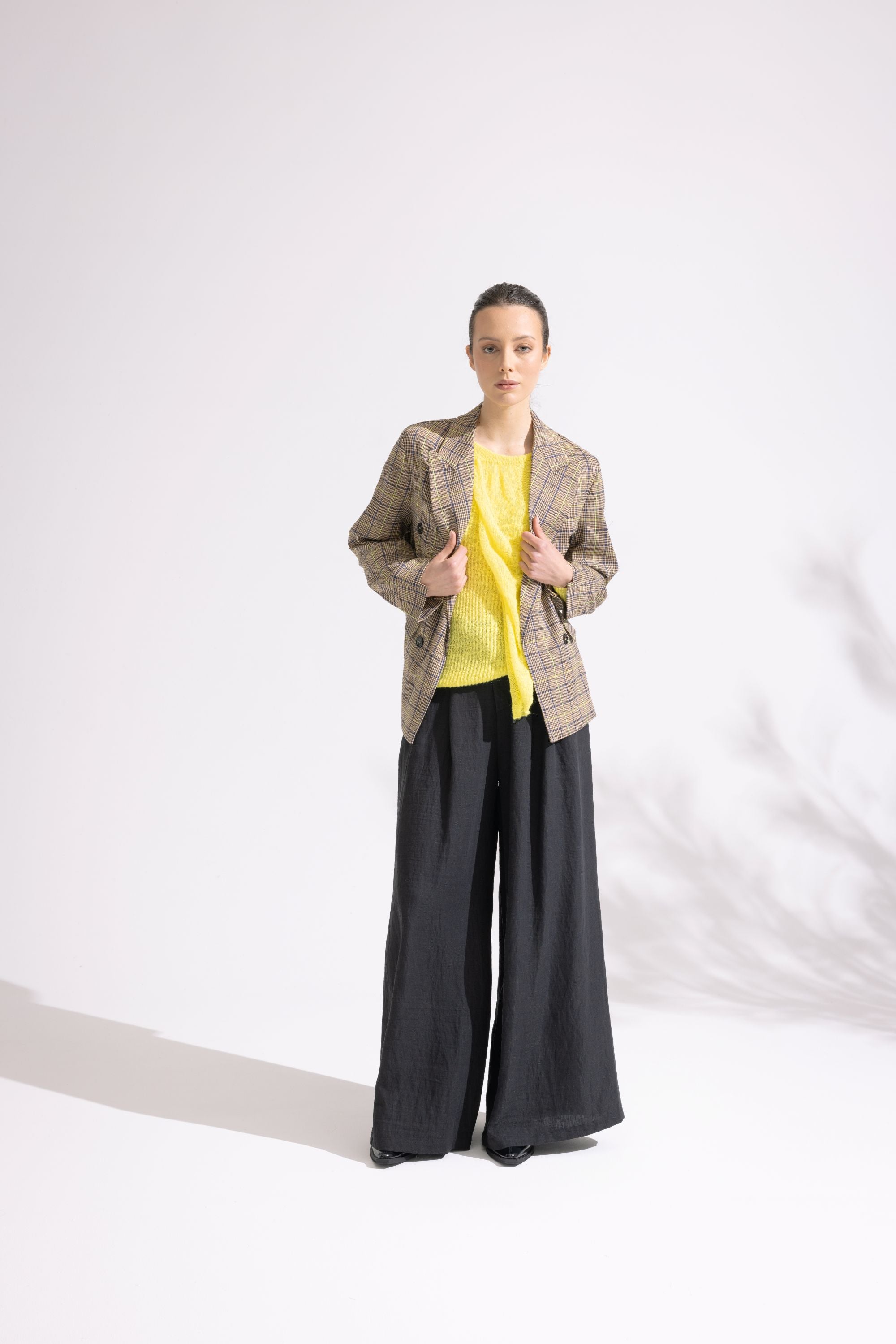 Person wearing a plaid jacket, yellow top, and black pants on a white background