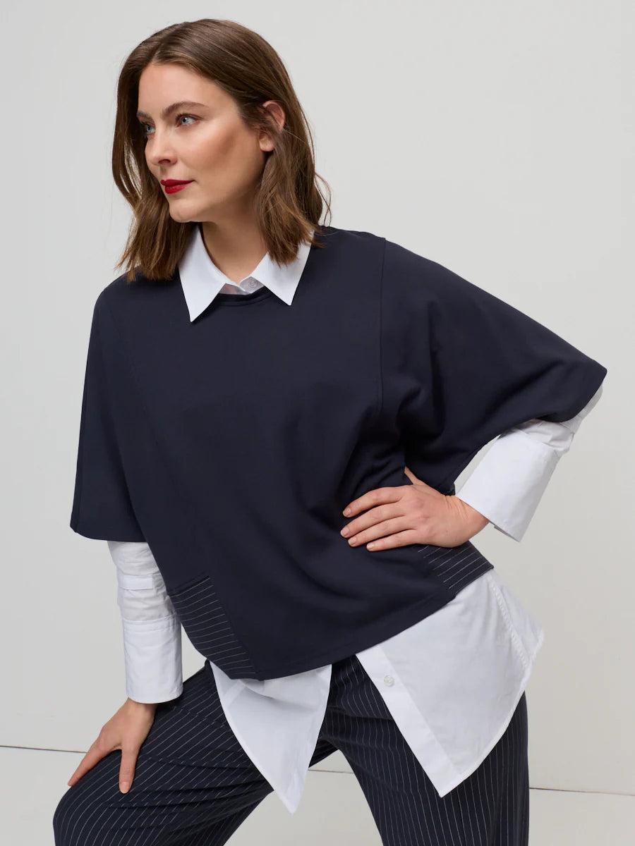 Woman wearing a navy sweater over a white shirt with a plain background