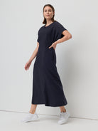 Woman wearing a dark blue dress with white sneakers on a light gray background