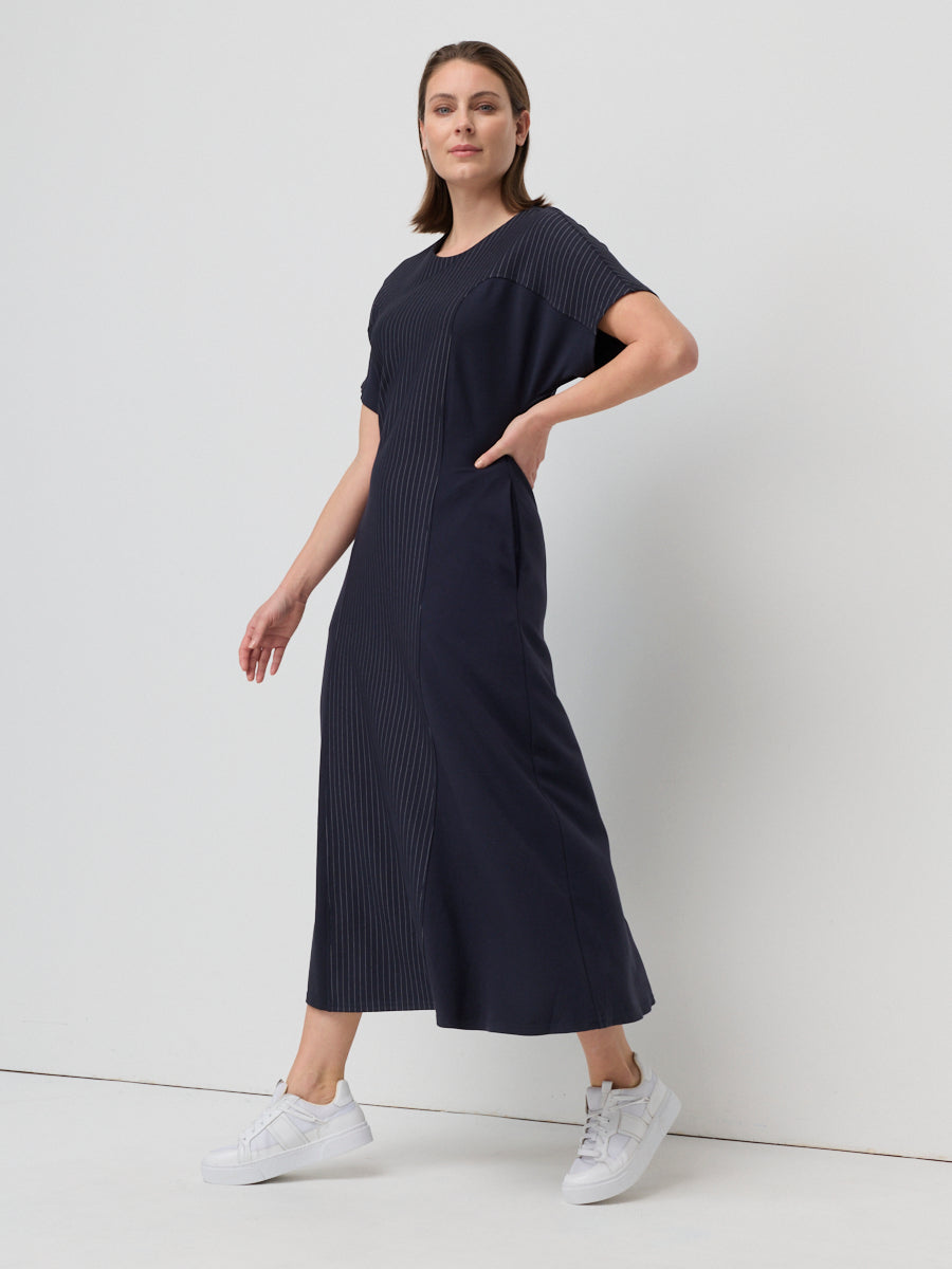 Woman wearing a dark blue dress with white sneakers on a light gray background