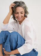 Woman wearing a white knit sweater and blue pants sitting on a white background