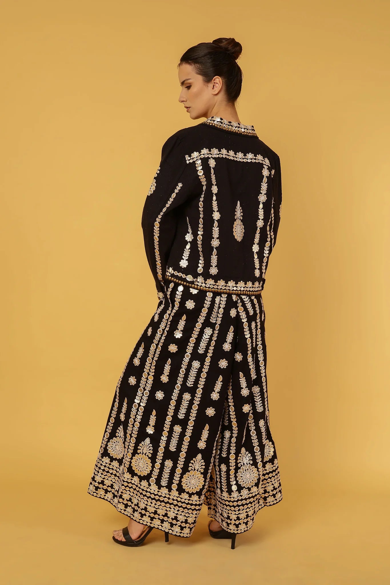 Woman wearing a black outfit with gold embroidery and mirrors on a beige background
