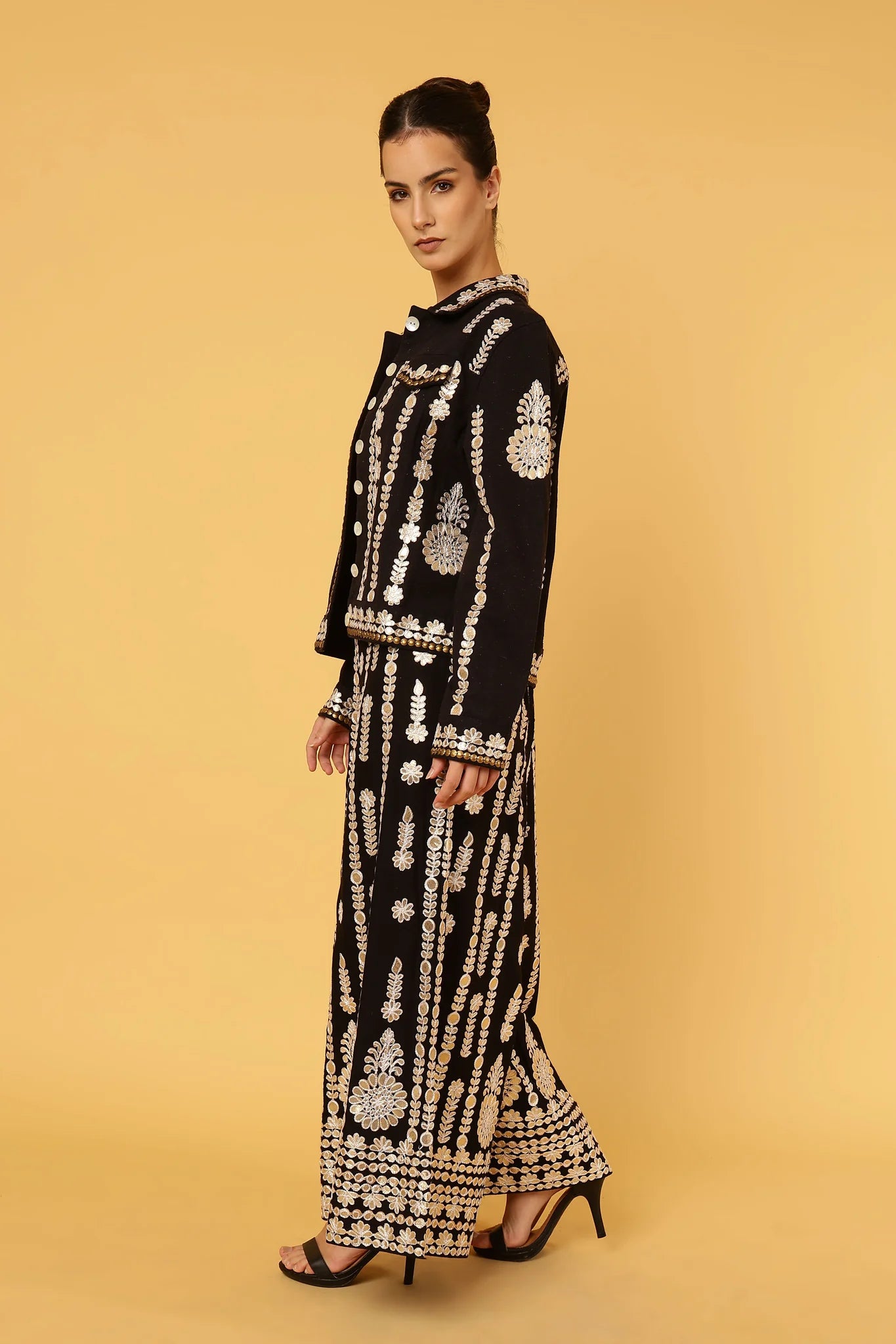 Woman wearing a black and gold embroidered outfit on a beige background