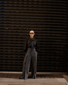 Person wearing a black shirt and gray pants standing in front of a dark metal shutter.