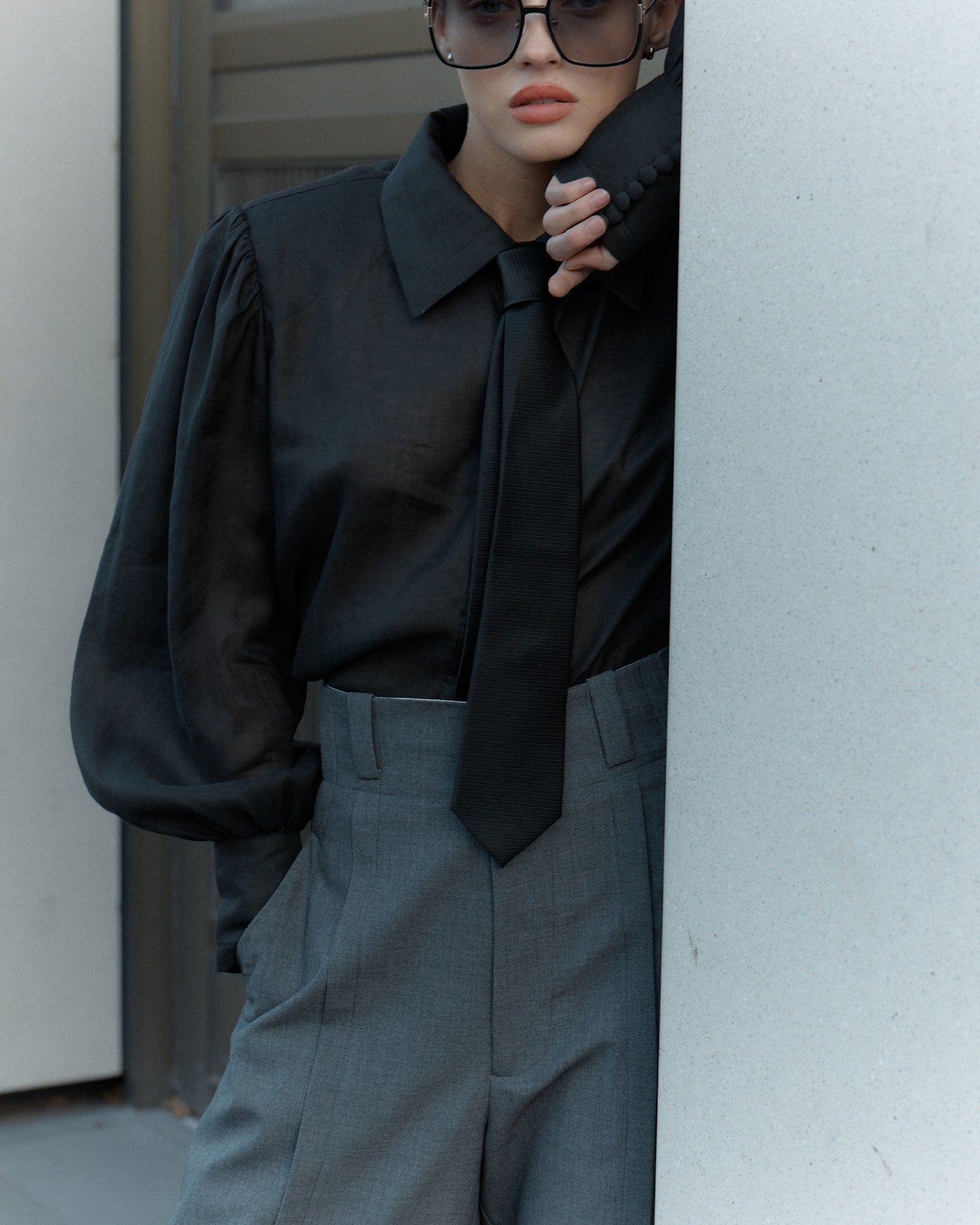 Person wearing a black shirt and gray pants peeking from behind a white wall.