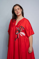 Woman wearing a v neck bright red midi length dress with elbow length sleeves and  flower motif against a white background.
