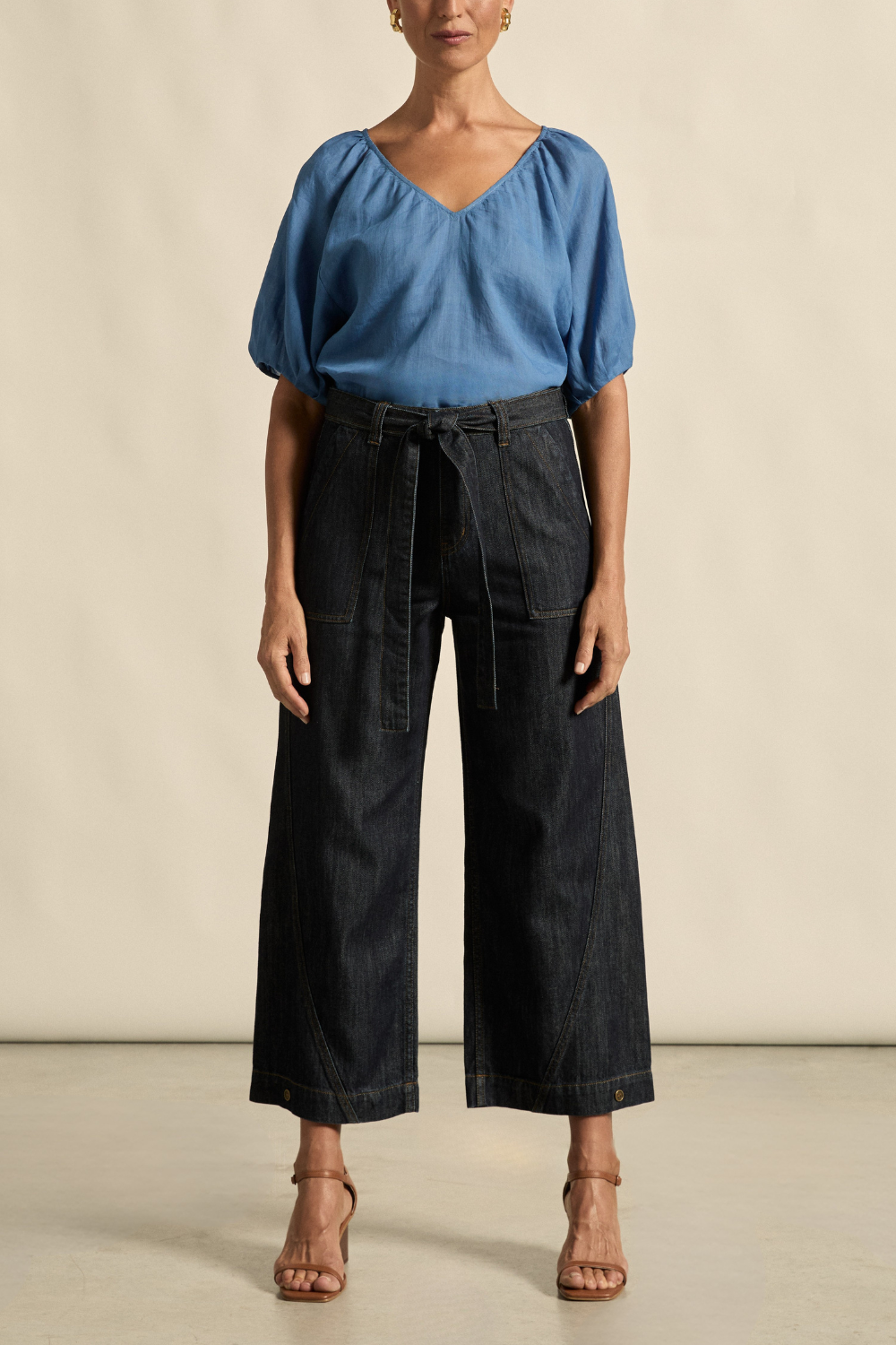 Woman wearing a blue blouse and dark denim wide-leg pants against a beige background