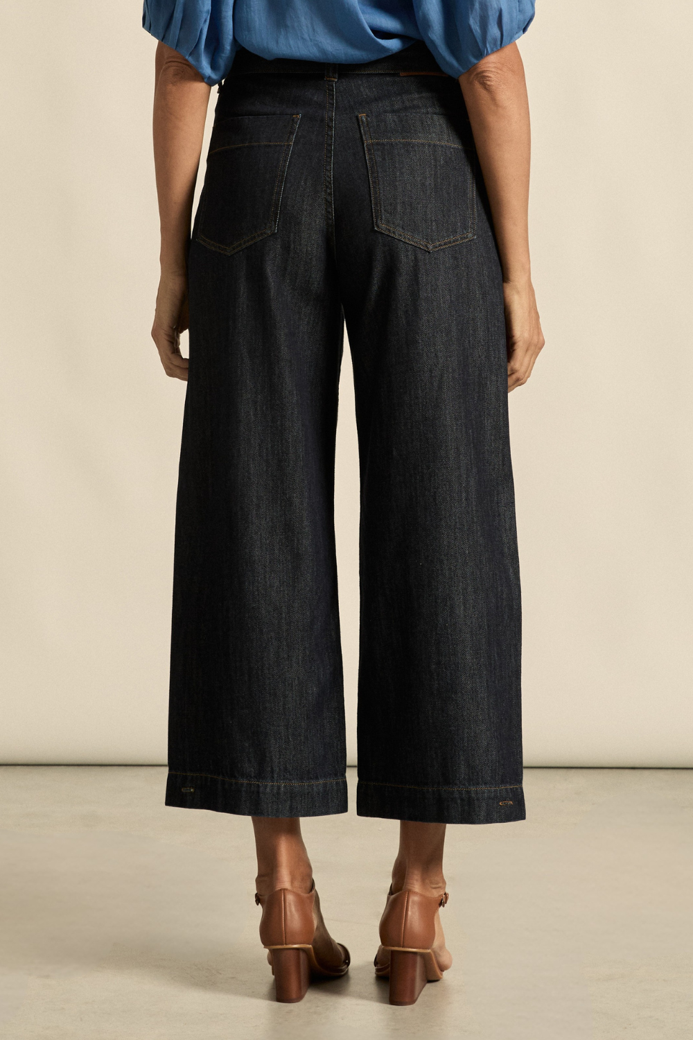 Person wearing black wide-leg jeans and a blue top on a neutral background