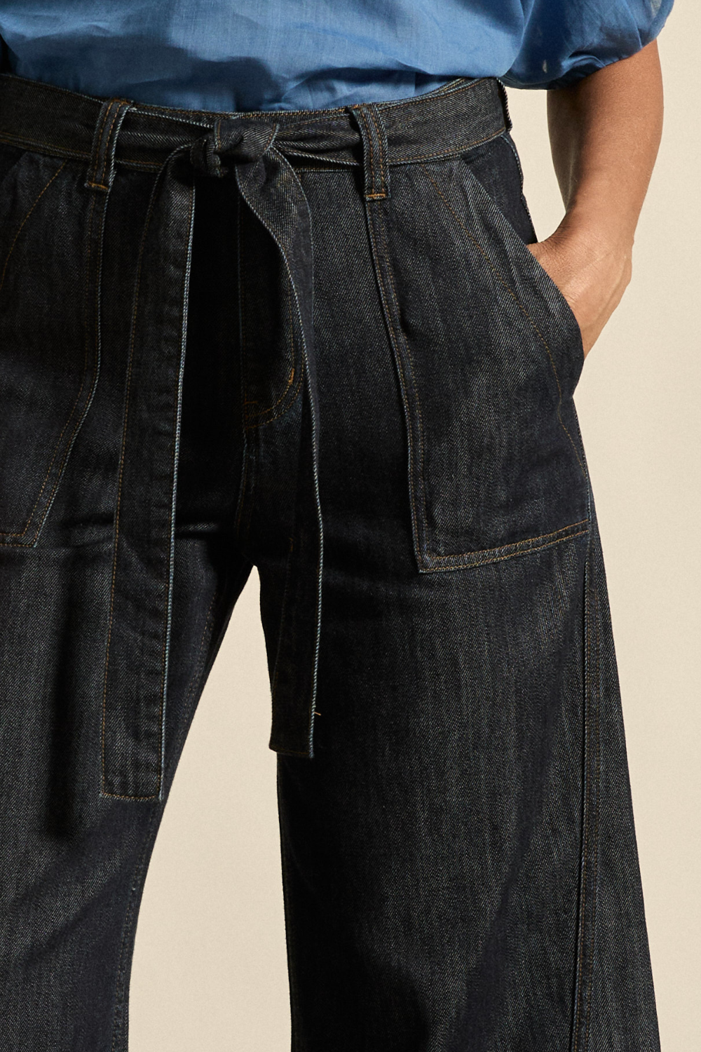 Person wearing dark denim pants with a belt on a beige background