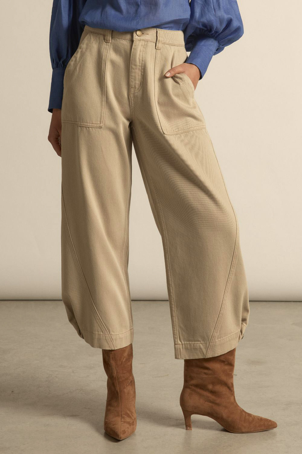 Person wearing beige pants and brown boots against a neutral background