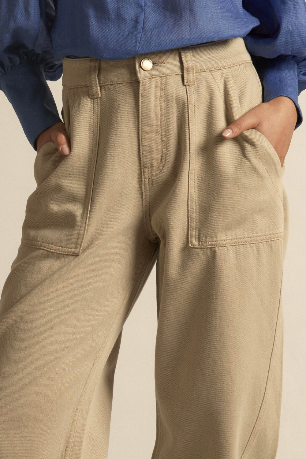 Beige pants worn with a blue shirt on a neutral background
