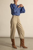 Person wearing a blue blouse, beige pants, and brown boots on a neutral background