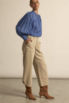 Woman wearing a blue blouse and beige pants against a neutral background