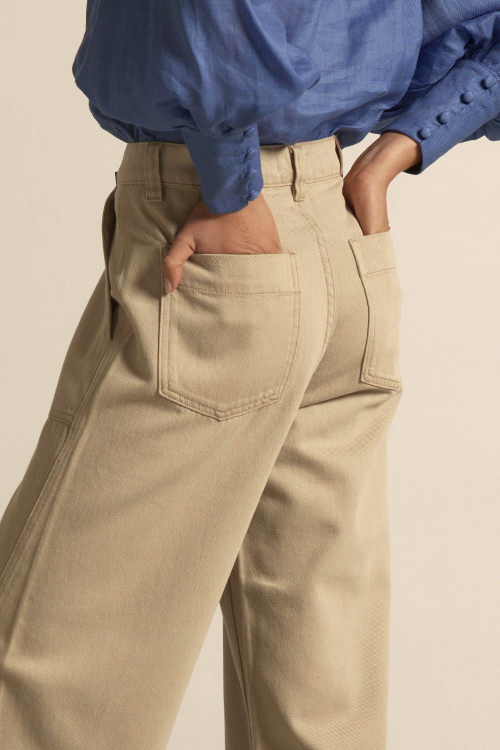 Person wearing beige pants and a blue shirt with a neutral background