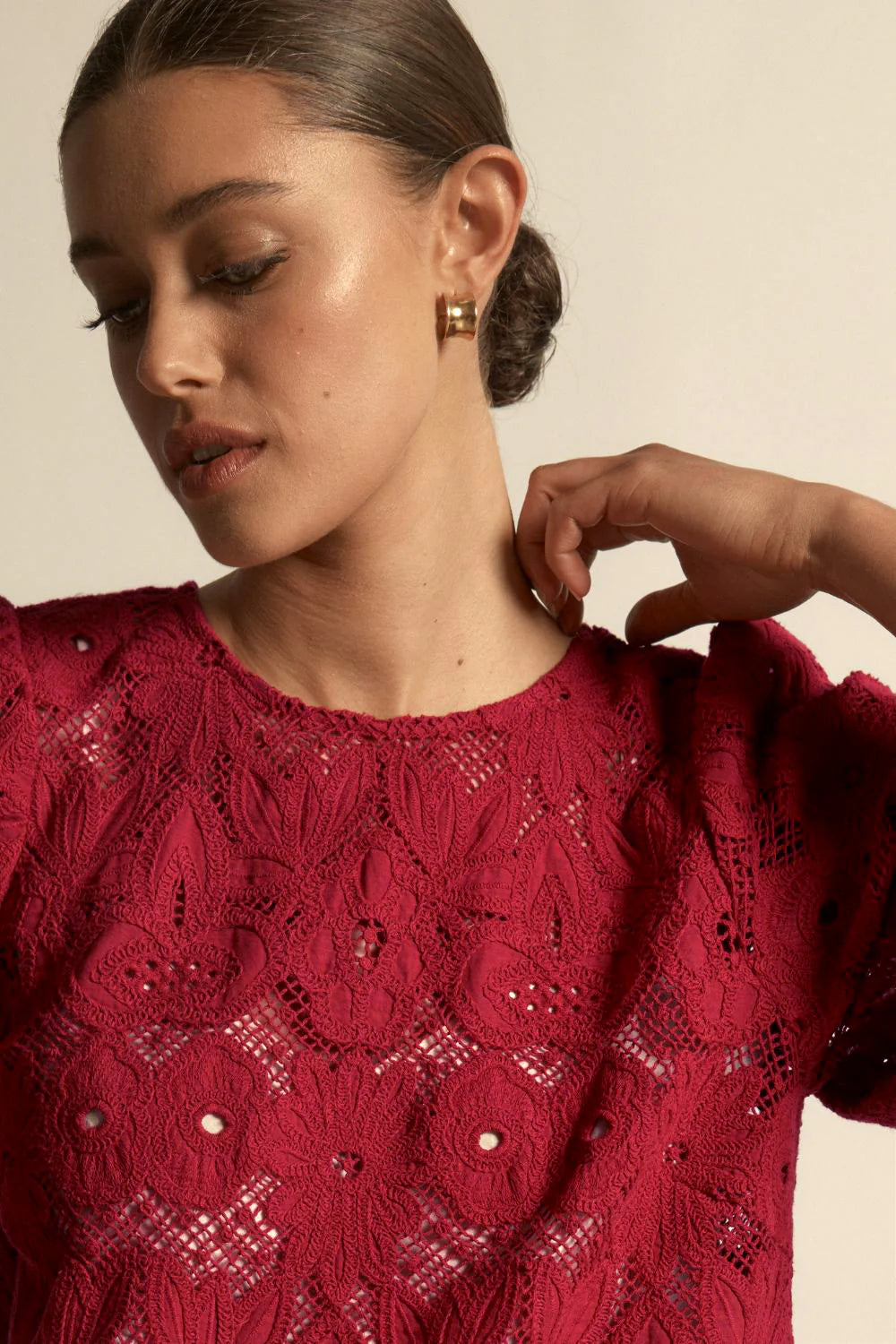 Woman wearing a red lace top with a neutral background