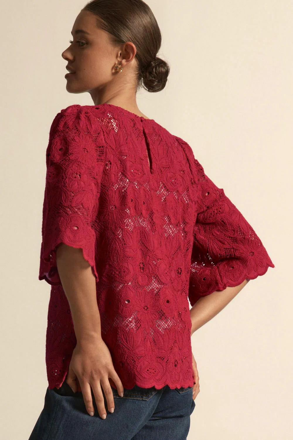 Woman wearing a red lace blouse against a beige background