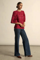 Woman wearing a red lace top and blue jeans against a beige background