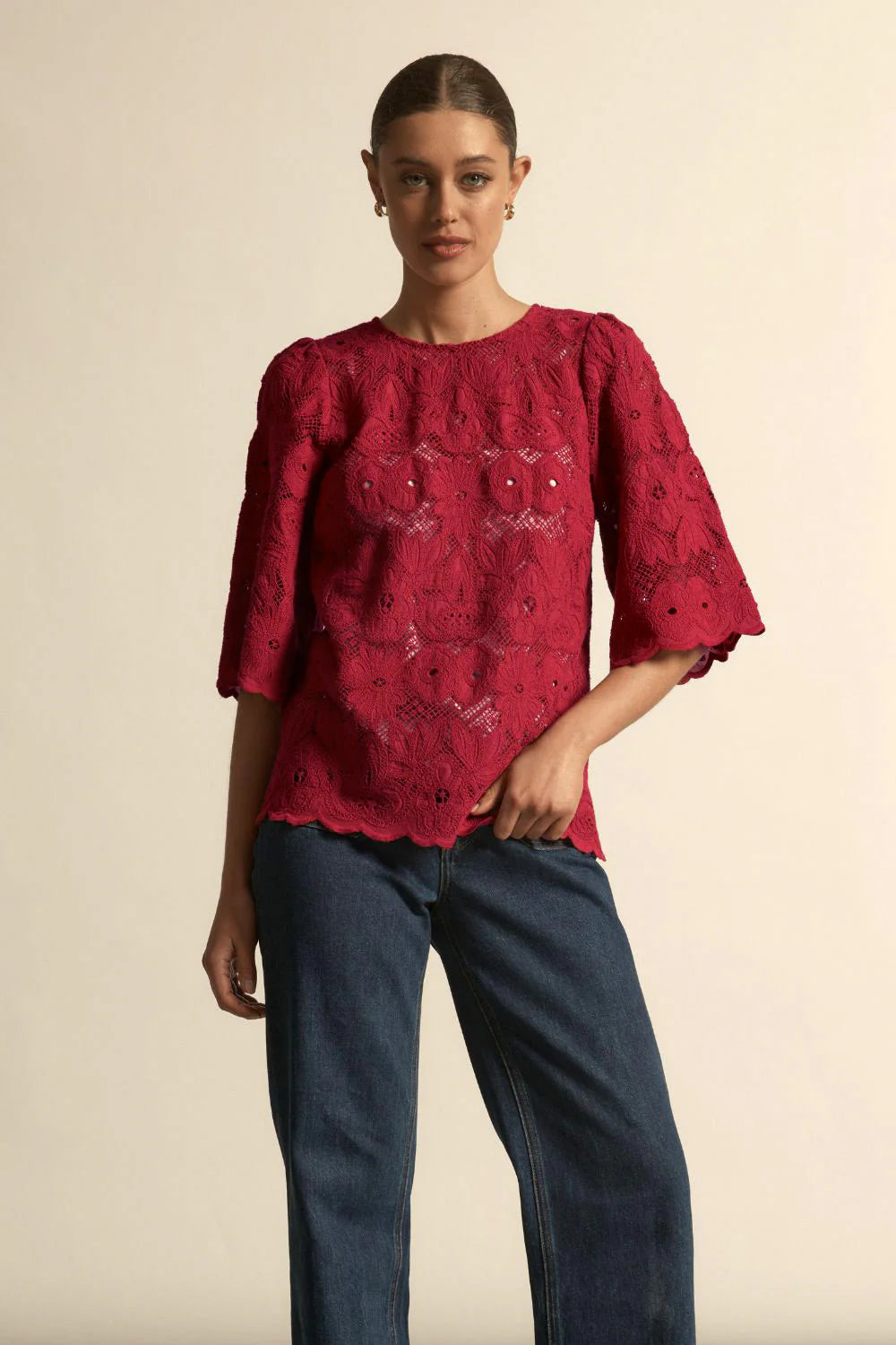 Woman wearing a red embroidered top and blue jeans against a beige background